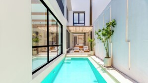 A narrow indoor swimming pool with clear blue water, surrounded by glass walls and a white exterior. - Villa Tin by Pertama Stay (Canggu)
