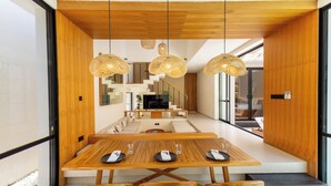 A modern dining area with a wooden table, chairs, and woven pendant lights. - Villa Tin by Pertama Stay (Canggu)