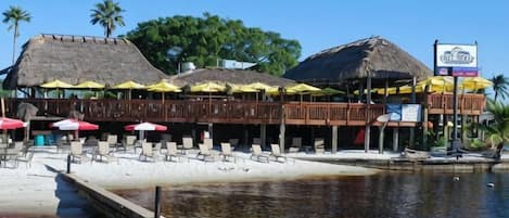 A beachfront restaurant with thatched roofs and outdoor seating.