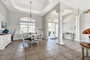 A spacious dining area with a round table and chairs, a chandelier, and a view through a window. - Boaters Dream, S. Terr, Pool, Yacht Club, Boating (Cape Coral)