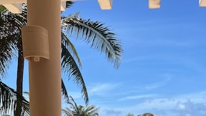 Un restaurante en la playa con un menú sobre la mesa, palmeras y una sombrilla de paja al fondo.