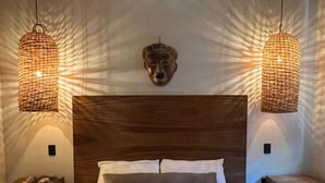 Un dormitorio con una cama grande, dos mesitas de noche, un aire acondicionado de pared y dos lámparas colgantes de mimbre.