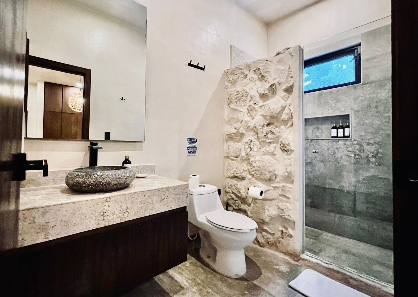 A modern bathroom with a stone sink, toilet, and a glass shower enclosure.