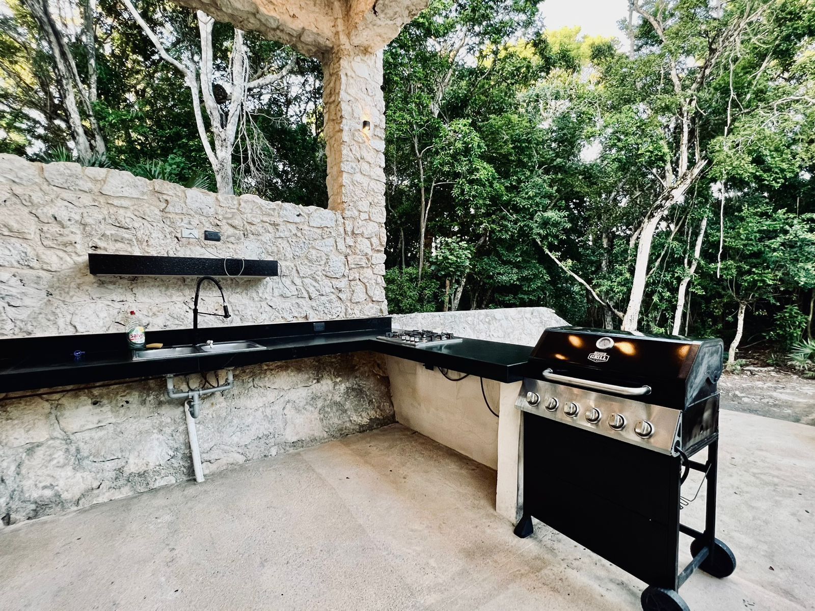 Una cocina al aire libre con pared de piedra, encimera negra y una parrilla portátil.