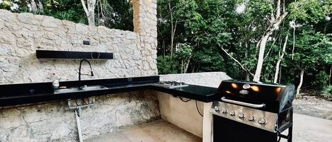 Una cocina al aire libre con pared de piedra, encimera negra y una parrilla portátil.