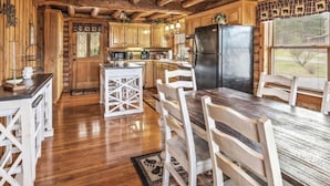 L’intérieur d’un chalet rustique, avec des poutres en bois, un coin cuisine et une table à manger entourée de chaises.
