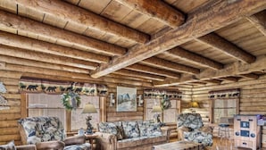L’intérieur d’une cabane en rondins, avec un plafond en bois, un ensemble de canapés, une table basse et une cheminée.
