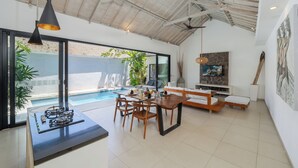 Une cuisine moderne équipée d’une cuisinière à gaz, d’une table à manger et de chaises en bois, un espace de détente au bord de la piscine avec un canapé et un téléviseur, et un ventilateur de plafond.