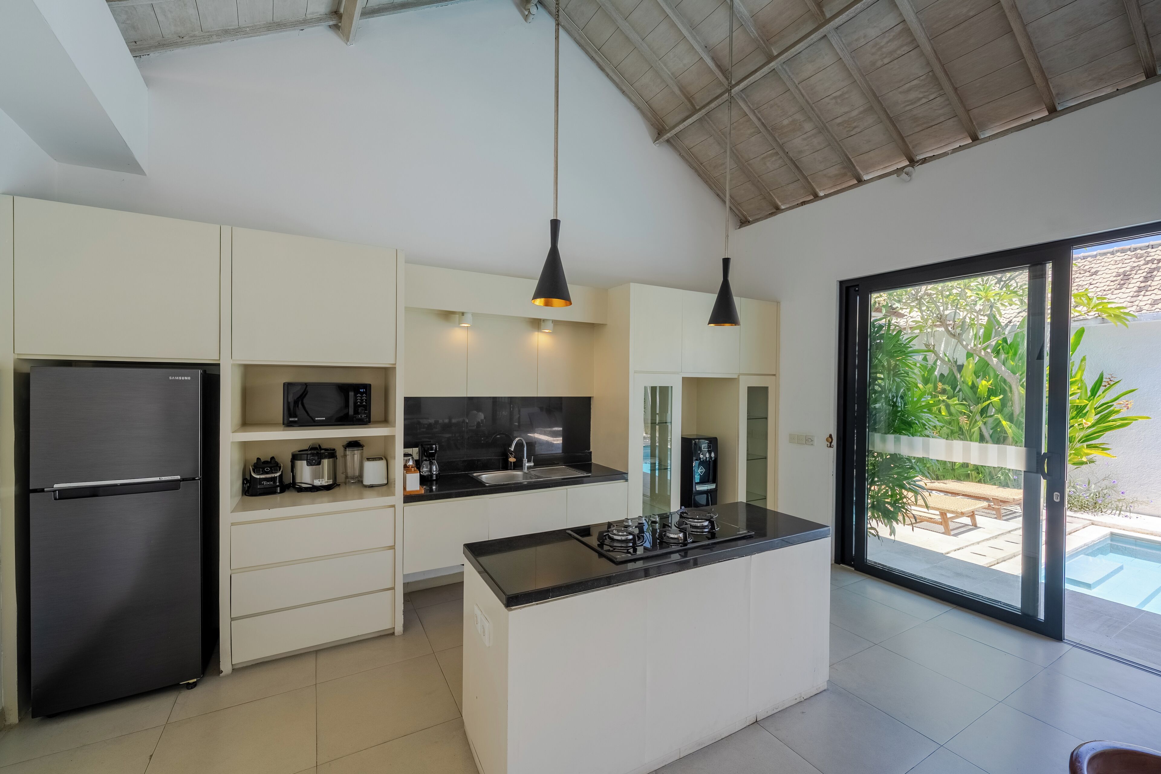 Une cuisine moderne dotée d’un réfrigérateur encastré, d’un îlot central avec une plaque de cuisson, de meubles blancs et de luminaires suspendus.