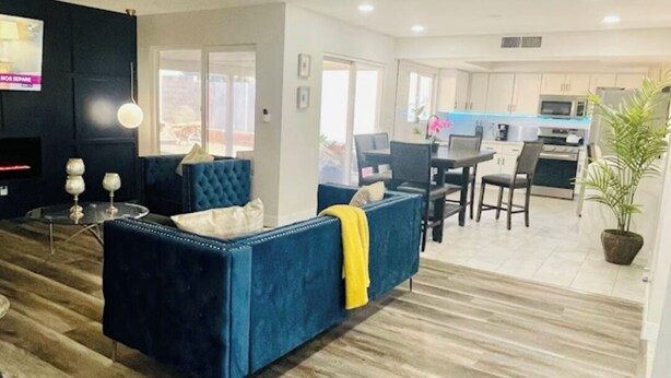 A modern living room with a blue sofa, a dining area, and a kitchen in the background. - Renovated 4BR Las Vegas Home Private Pool, BBQ Ping Pong Parking 20 min to Strip (Henderson)