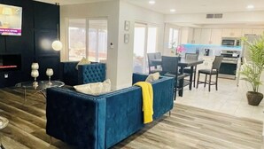 A spacious living area with a blue sofa, a dining table, and a kitchen in the background. - Renovated 4BR Las Vegas Home Private Pool, BBQ Ping Pong Parking 20 min to Strip (Henderson)