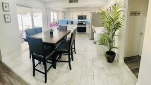 A modern kitchen with white cabinets, a microwave, and a sink. There is a dining area with a table and chairs, and a potted plant. - Renovated 4BR Las Vegas Home Private Pool, BBQ Ping Pong Parking 20 min to Strip (Henderson)