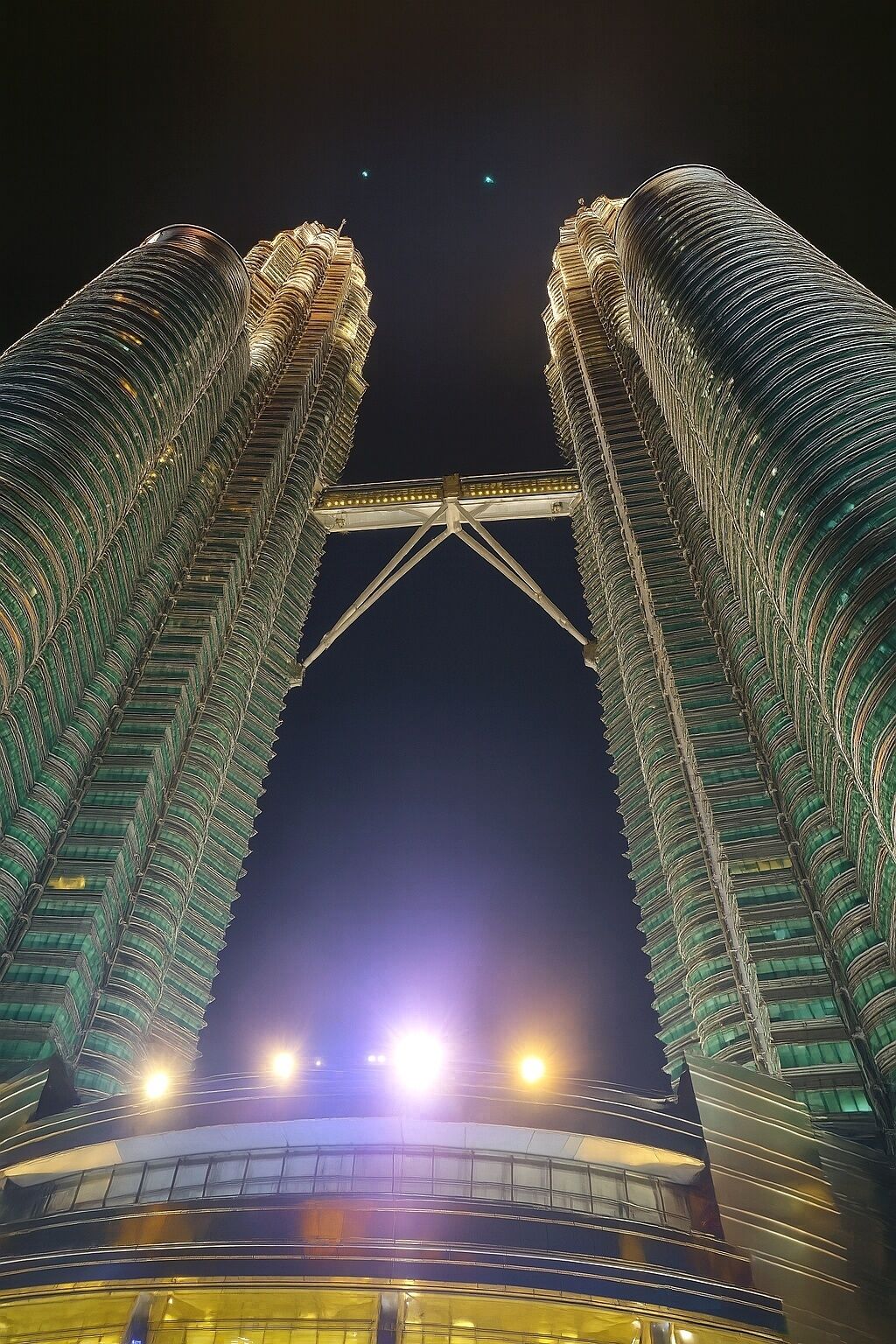 A night view of a large, modern building with two prominent towers connected by a bridge.