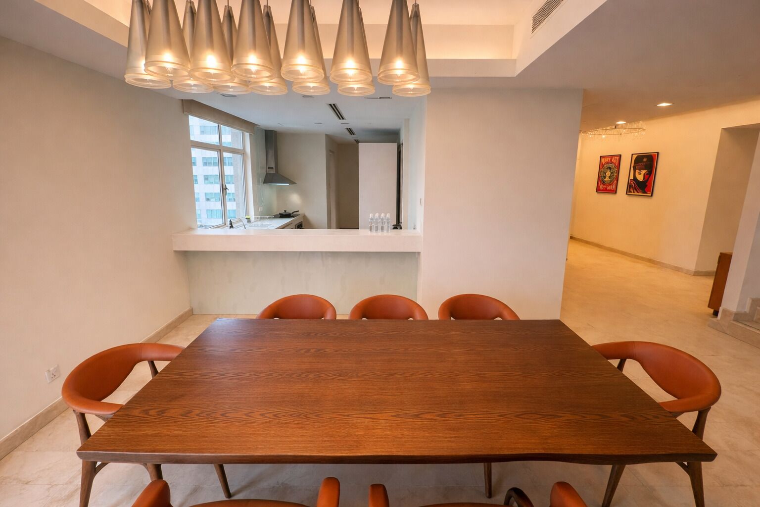 Un comedor con una mesa de madera y sillas anaranjadas, una lámpara colgante moderna y vistas a la cocina.