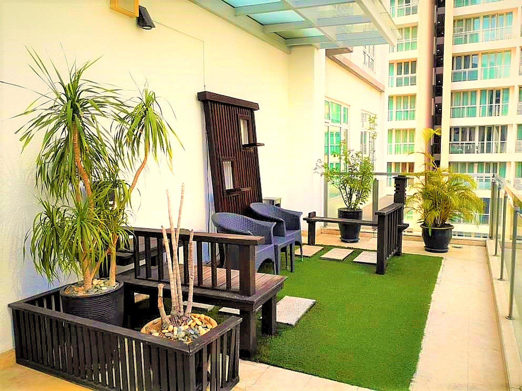Un jardín en la azotea con plantas en macetas, mobiliario exterior y vistas a un edificio moderno.