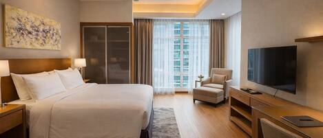 A hotel room with a large bed, a desk with a TV, a chair, and a ceiling fan.
