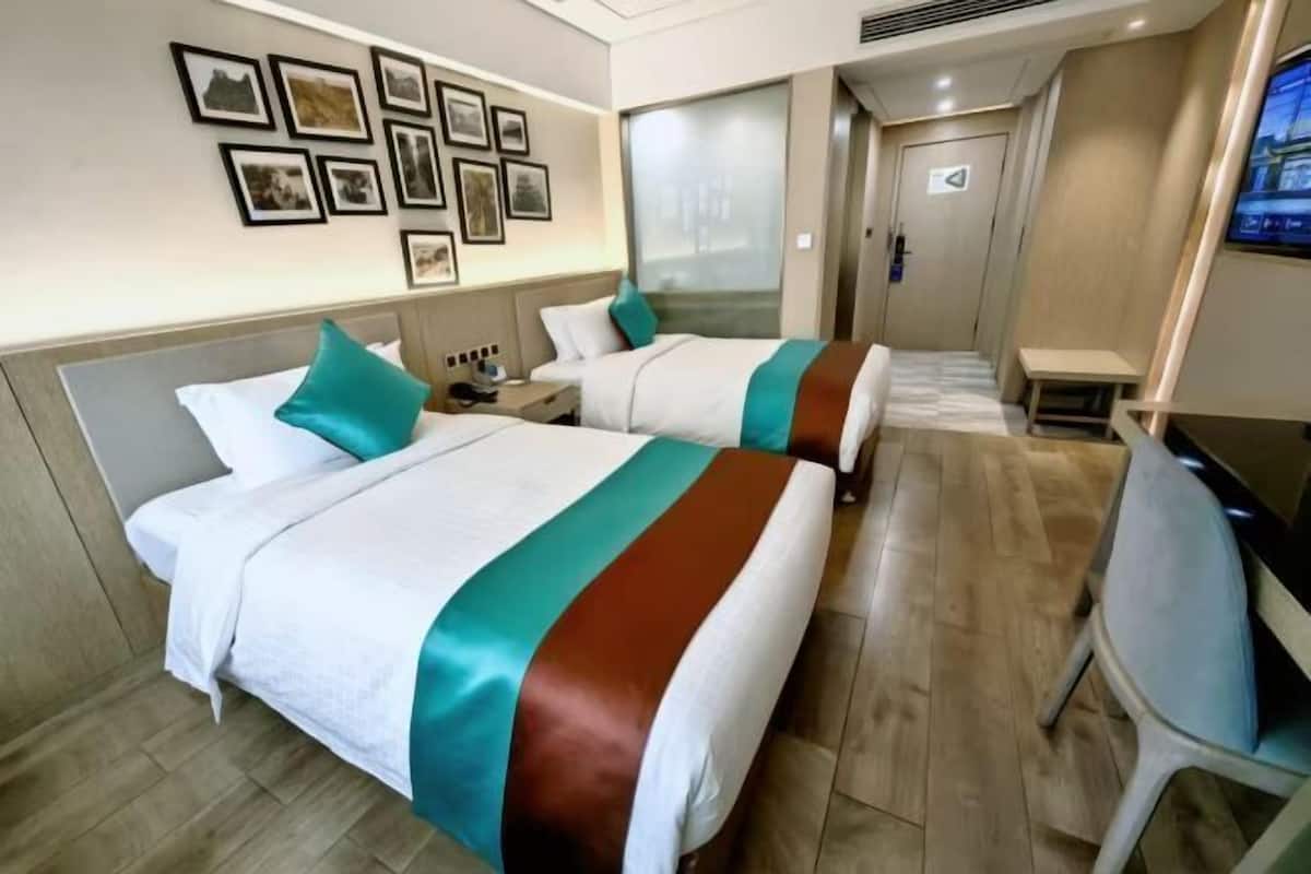 Ein Hotelzimmer mit zwei Betten, einem Schreibtisch, einem Stuhl, einem Fernseher und gerahmten Bildern an der Wand.