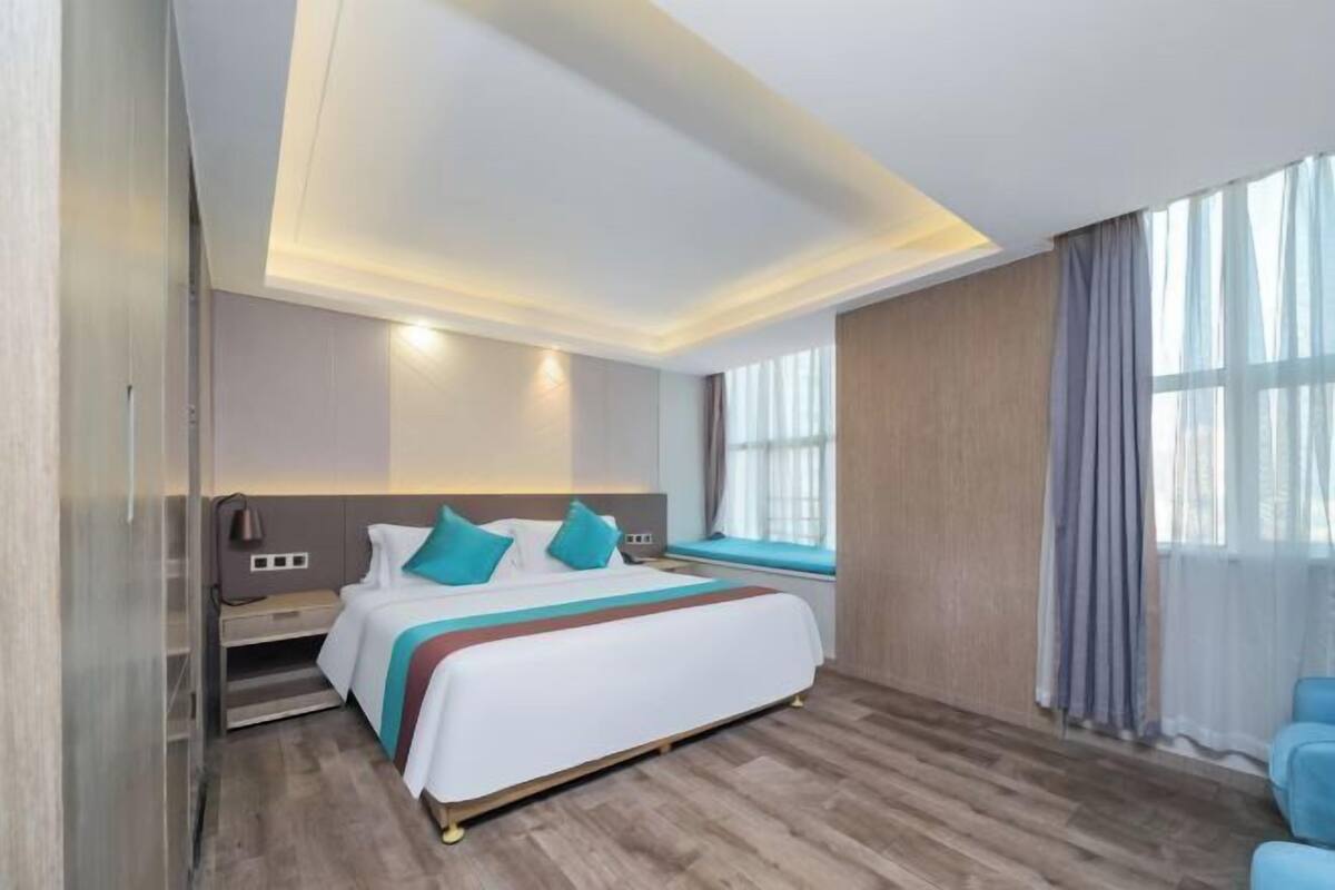 Ein modernes Hotelzimmer mit einem großen Bett, Nachttischen, einem Vorhangfenster und einem integrierten Schreibtisch.