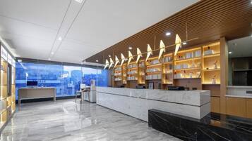 Un moderno vestíbulo de hotel con un mostrador de recepción de mármol, estanterías de madera con libros y vistas a la ciudad.