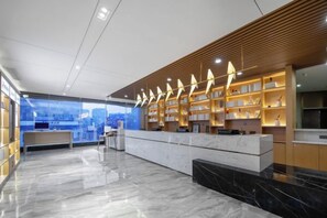 A modern hotel lobby with a marble reception desk, wooden shelving with books, and a city view. - Licheng Hotel (Wuhan Hankou Financial Center Wansongyuan Food Street) (Wuhan)