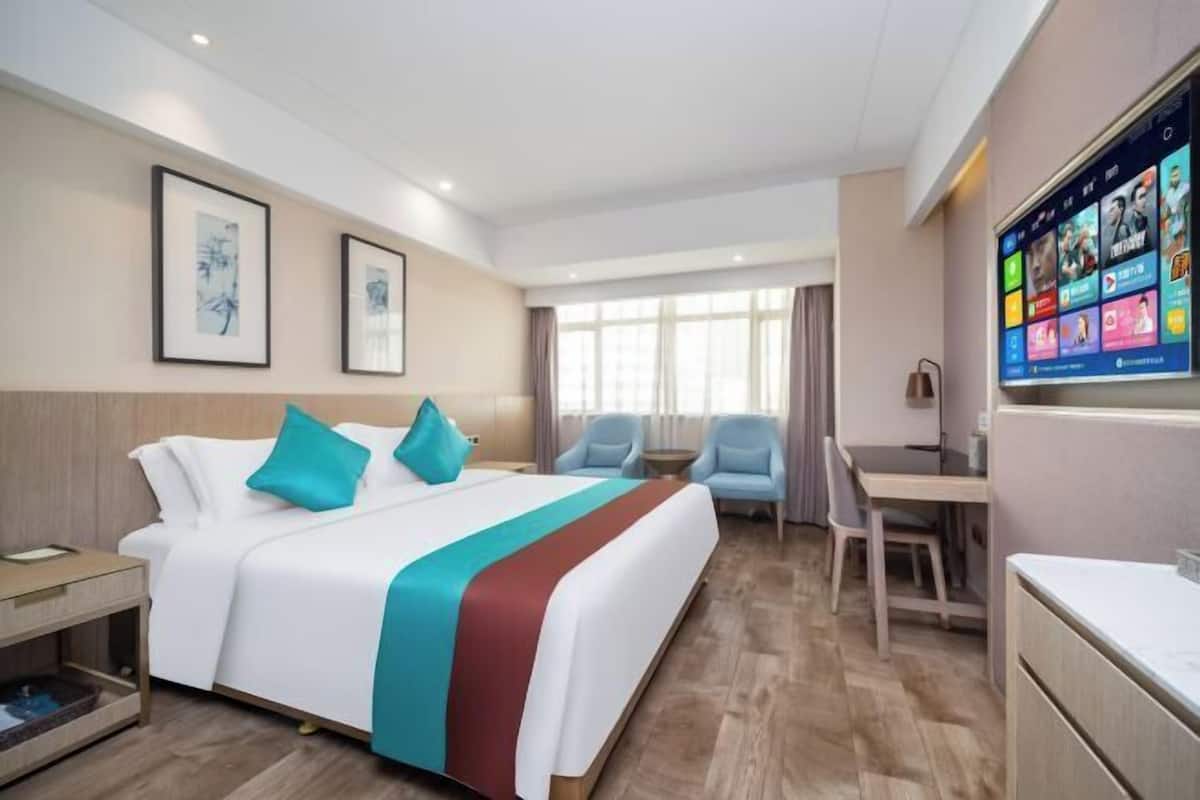 Ein Hotelzimmer mit Bett, Schreibtisch, zwei Stühlen, Fernseher und Bildern an der Wand.