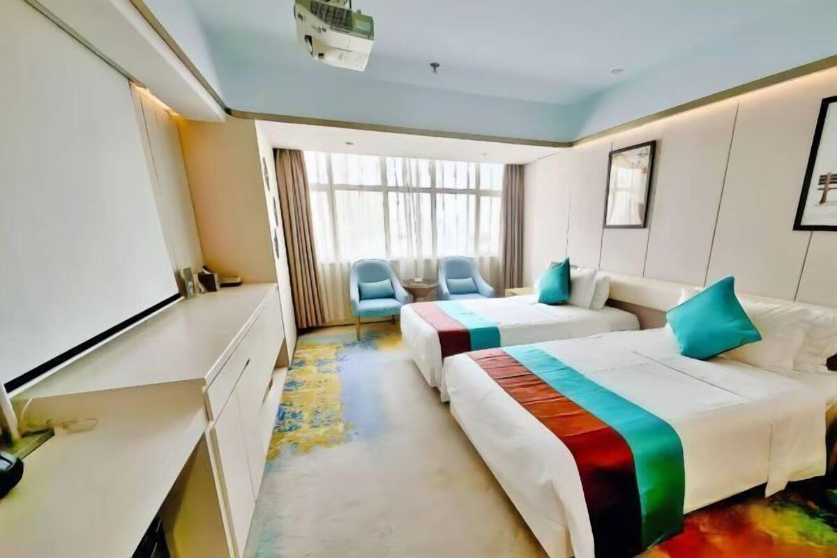 Ein Hotelzimmer mit zwei Betten, einem Schreibtisch, einem Stuhl und einem großen Fenster.