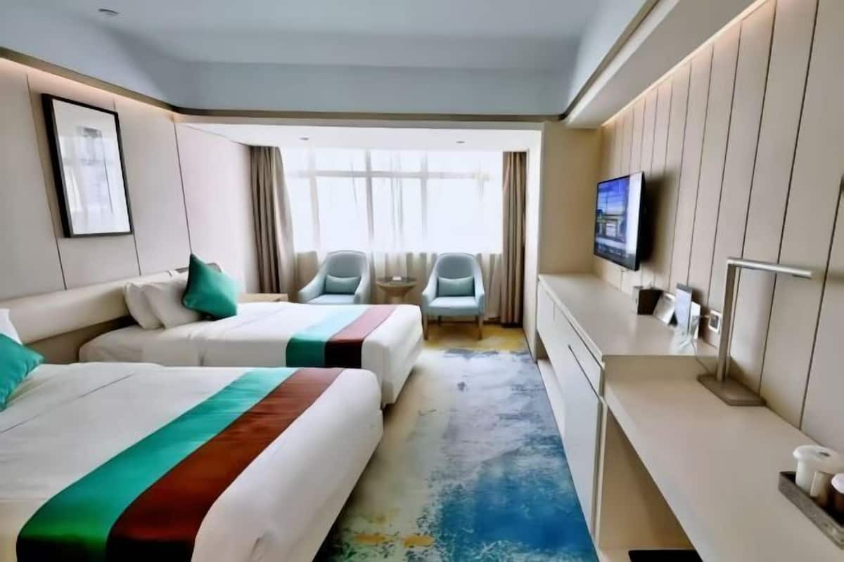 Ein Hotelzimmer mit zwei Betten, einem Schreibtisch, einem Fernseher und einem Fenster mit Vorhängen.