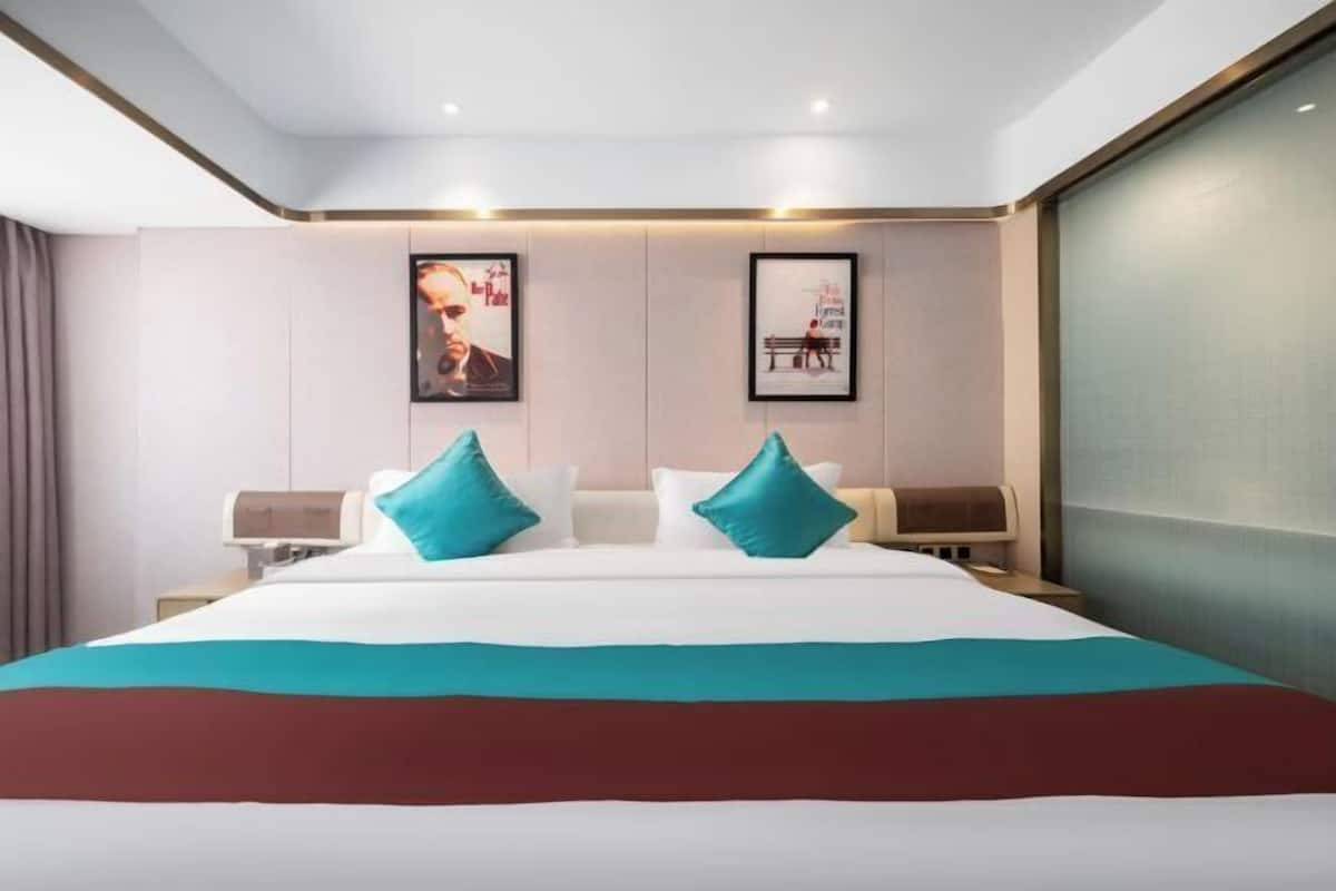 Ein Hotelzimmer mit einem großen Bett, zwei Nachttischen, einem an der Wand befestigten Fernseher und gerahmten Kunstwerken.