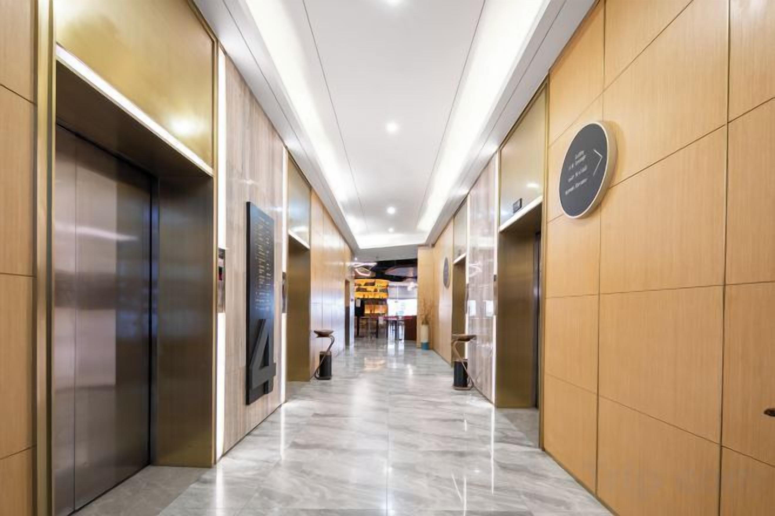 A hotel corridor with elevators, a reception area, and a polished marble floor.