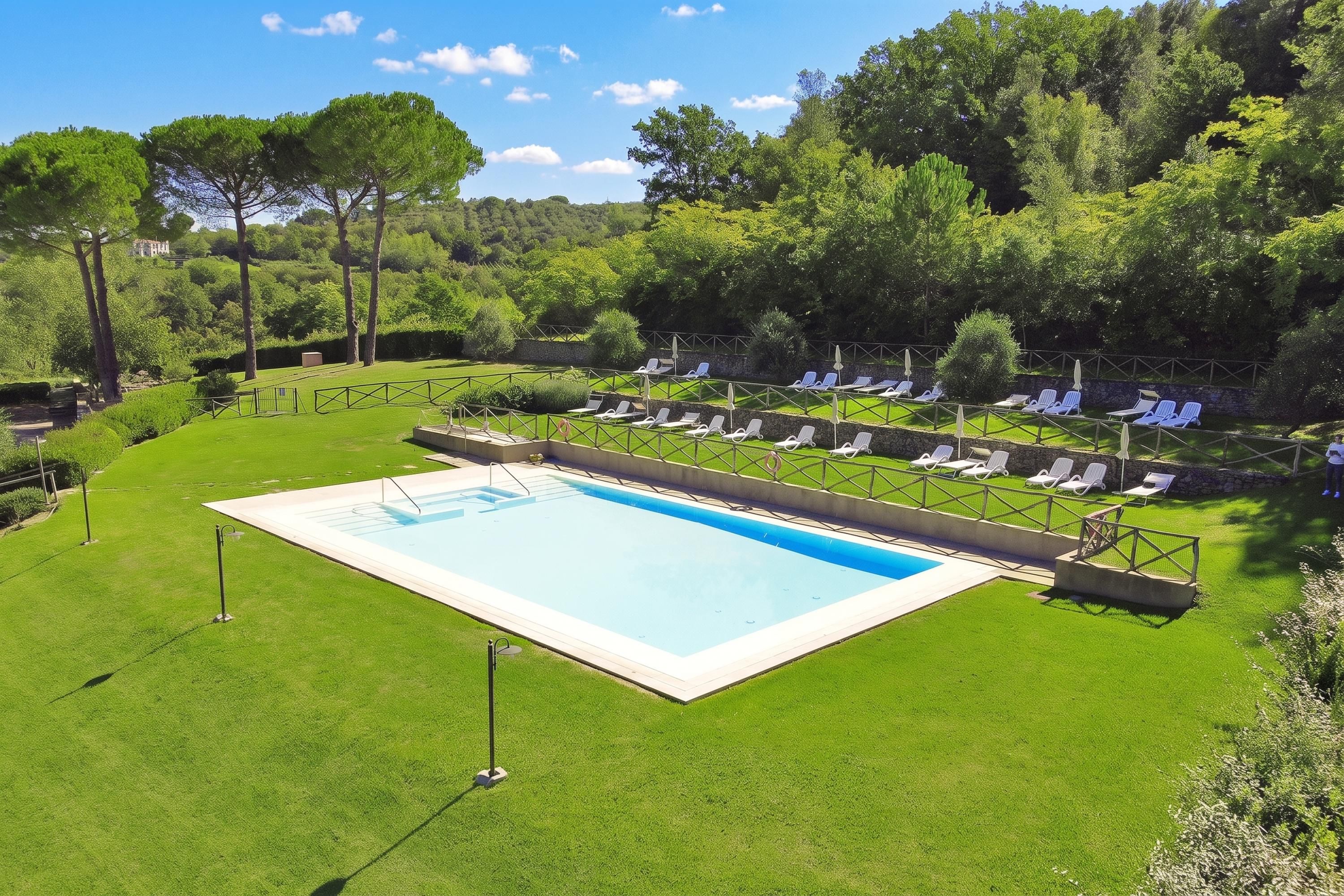 Una piscina rodeada de césped, sillas de descanso y un muro de piedra.