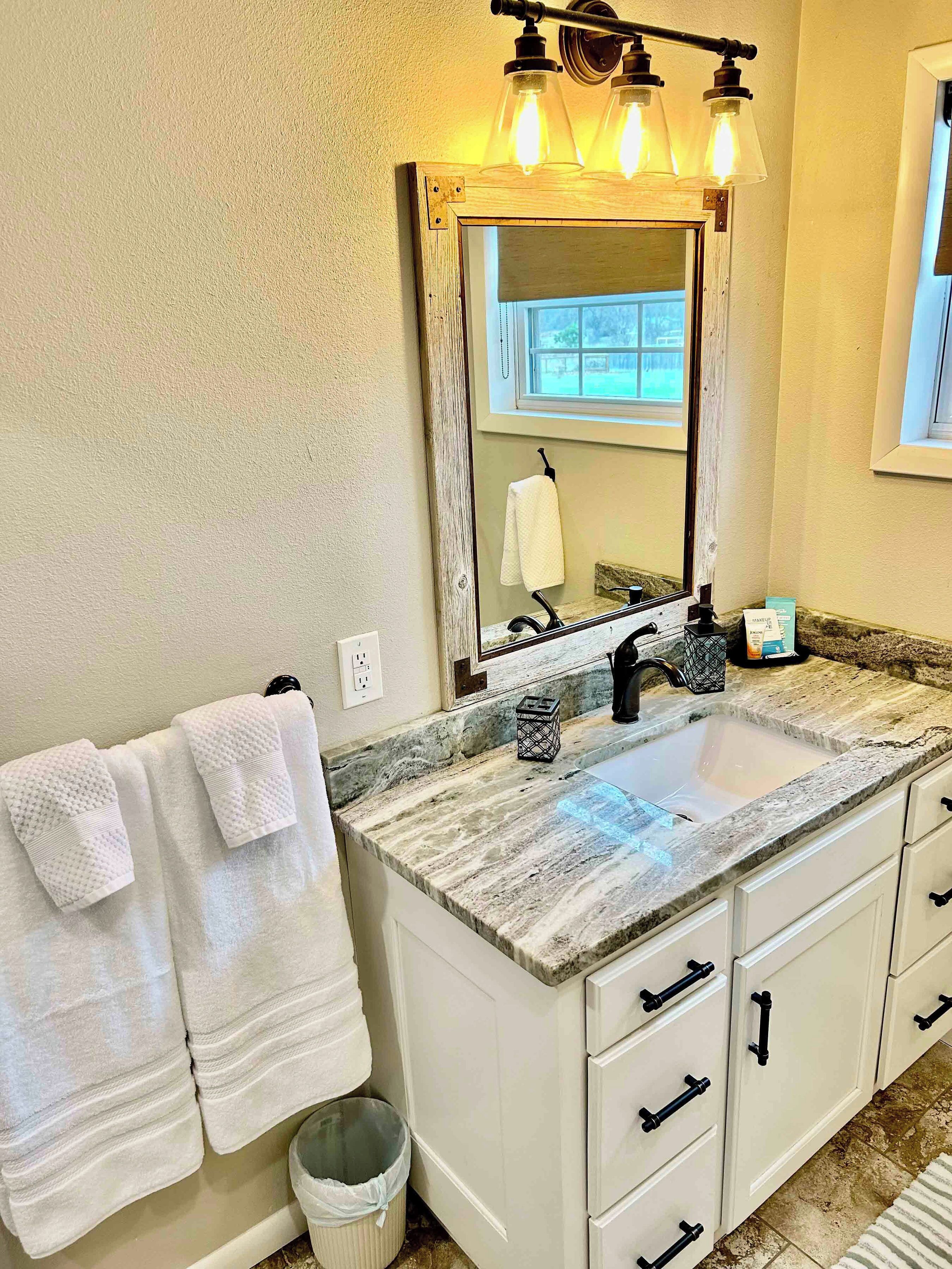 Une salle de bain avec un double lavabo, des meubles blancs, un miroir avec un cadre en bois et un porte-serviettes avec deux serviettes.