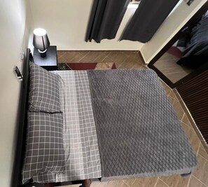 A bed with a checkered bedspread and pillows, a bedside table with a lamp, and a textured rug on the floor.