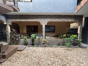 A courtyard with a stone wall, potted plants, and a pebbled ground.