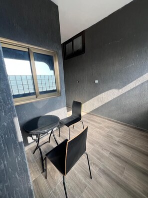 A room with a round table and two chairs, a window with a view, and a textured wall.
