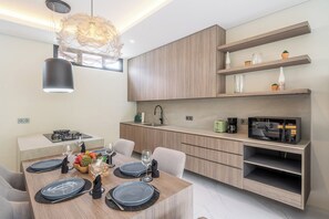 Une cuisine moderne avec des meubles en bois, une table à manger pour quatre personnes et un four à micro-ondes encastré.