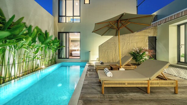 A modern outdoor pool area with lounge chairs and an umbrella, surrounded by plants and a stone wall. - Villa Noema 2 - Brand New 2BR Villa with Pool (Badung)