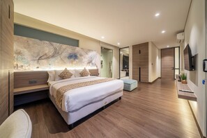 Une chambre moderne avec un grand lit, une table de chevet, un téléviseur fixé au mur et une salle de bain visible à travers une porte ouverte.