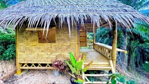 Une cabane au toit de chaume, avec un plancher en bois et un petit porche.