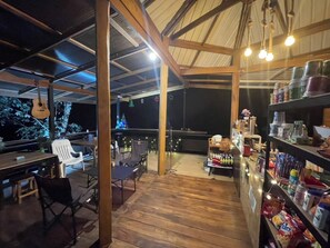 Un patio al aire libre con suelo de madera, mesas, sillas y varios alimentos y bebidas en estanterías.