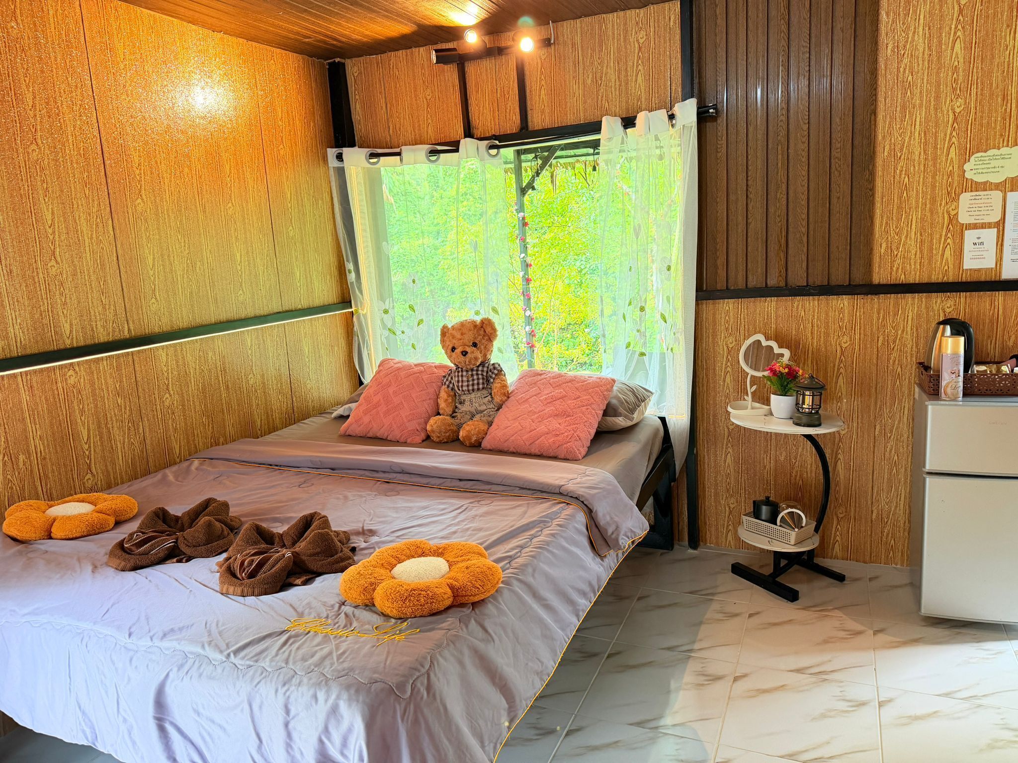 A bedroom with a bed, a teddy bear, pillows, a small table with a mirror, and a white cabinet.