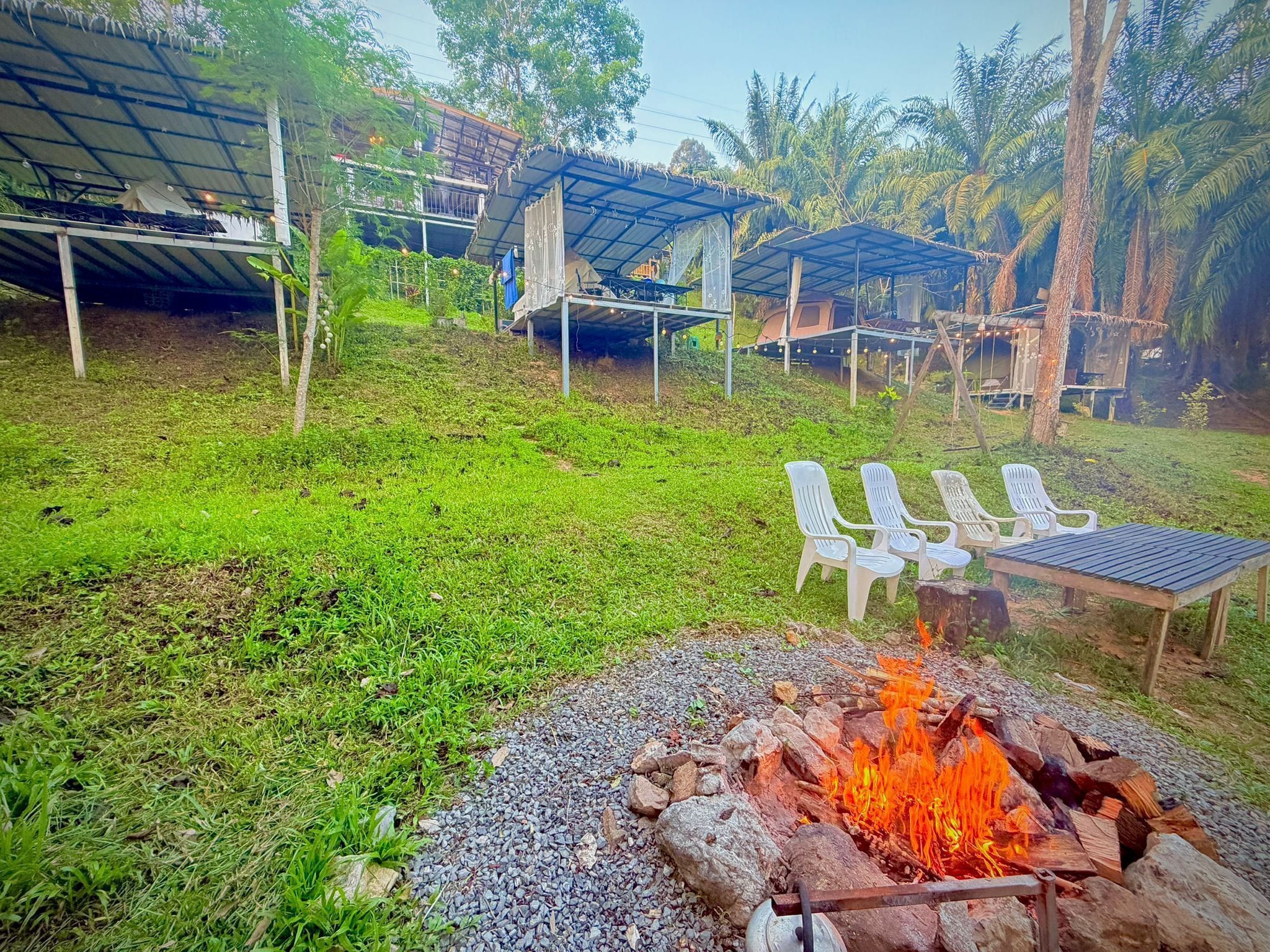 A campsite with a fire pit, outdoor seating, and covered structures.