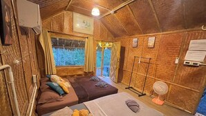 Une chambre confortable avec deux lits, un ventilateur sur pied et une fenêtre avec des rideaux.