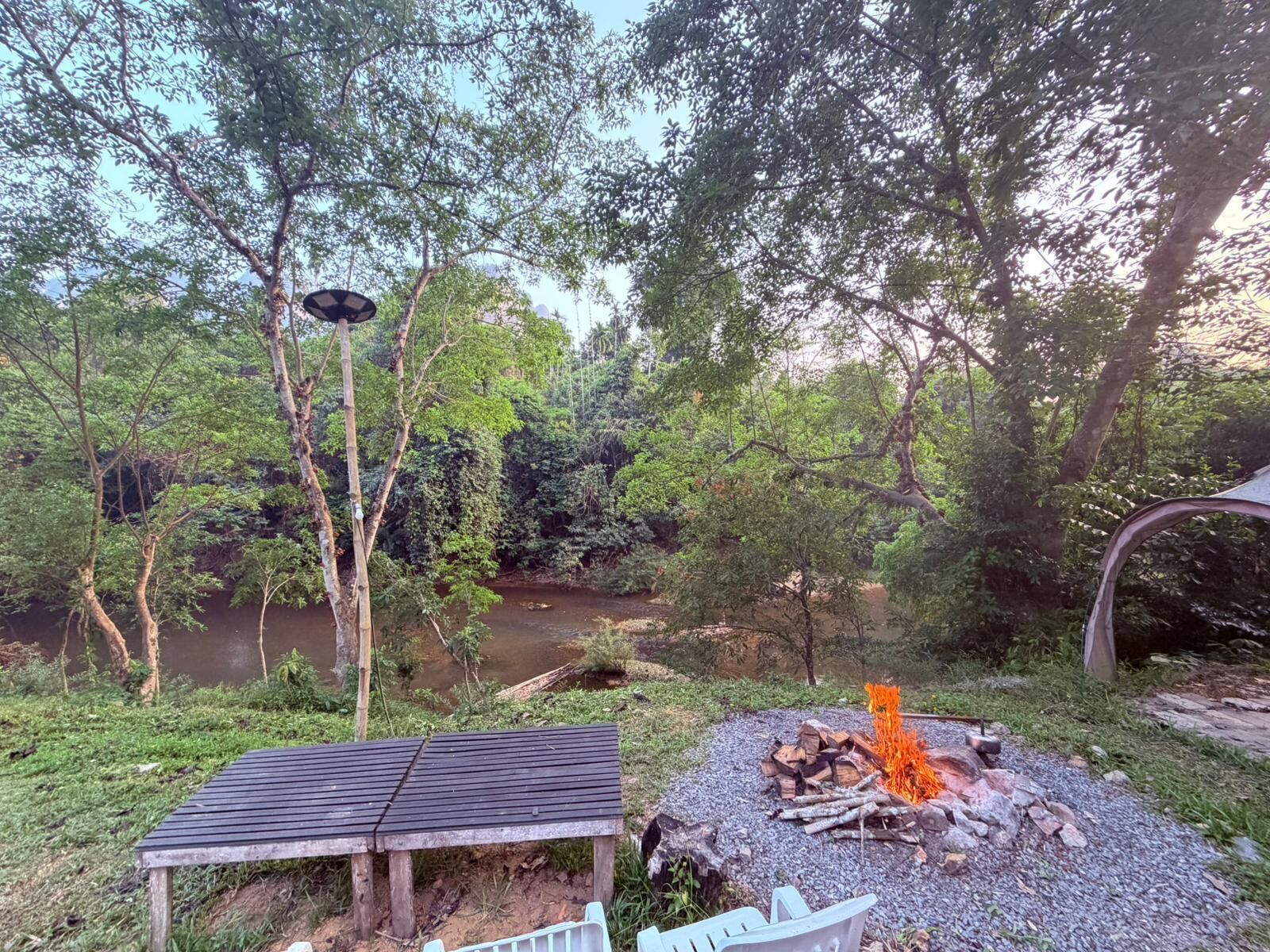 Un banc en bois, un foyer et une rivière, le tout situé dans une zone boisée.