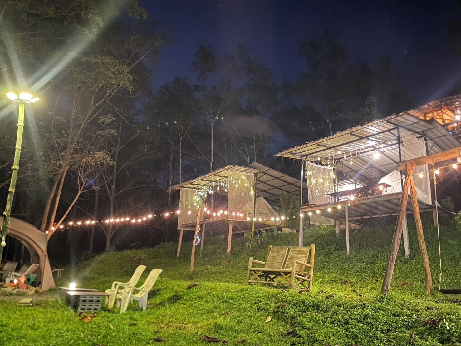 En campingplats med tält och en träbänk, omgiven av grönska och ljusslingor.