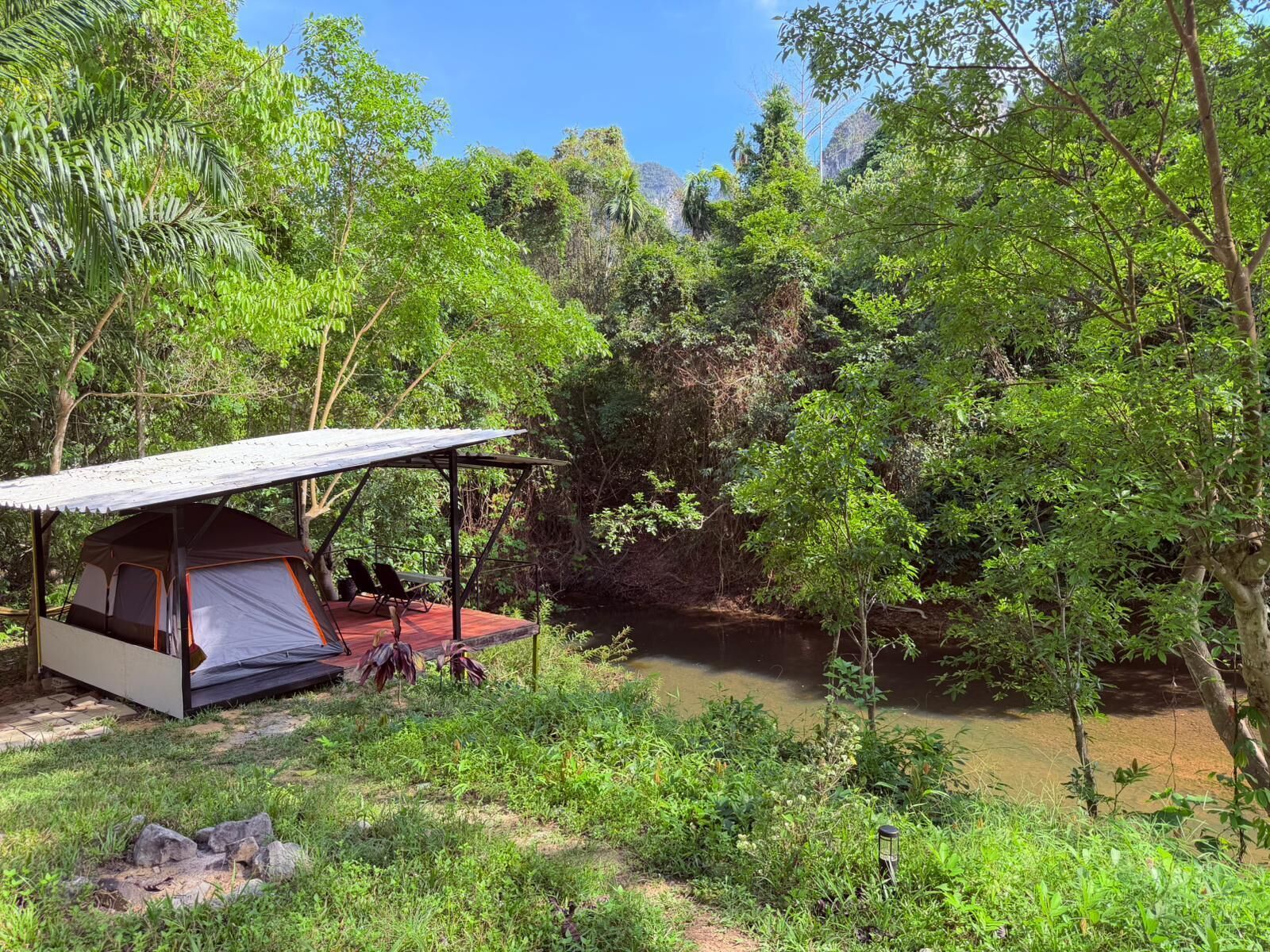 A tented camping area with a view of a river and dense forest.
