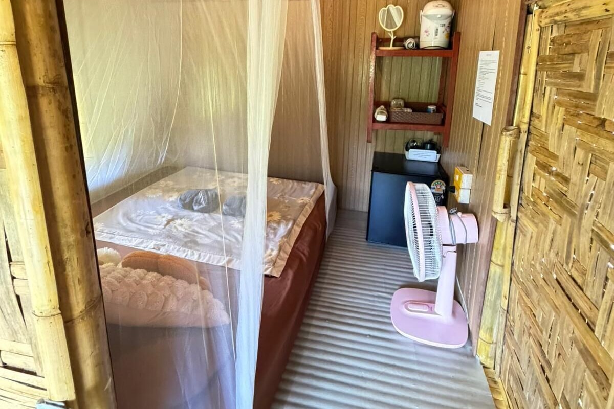 A small, cozy room with a bed, a bedside table, a mirror, and a fan.