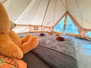 Een tent met een pluche speeltje, een deken met sneeuwvlokpatronen, en uitzicht op groen.