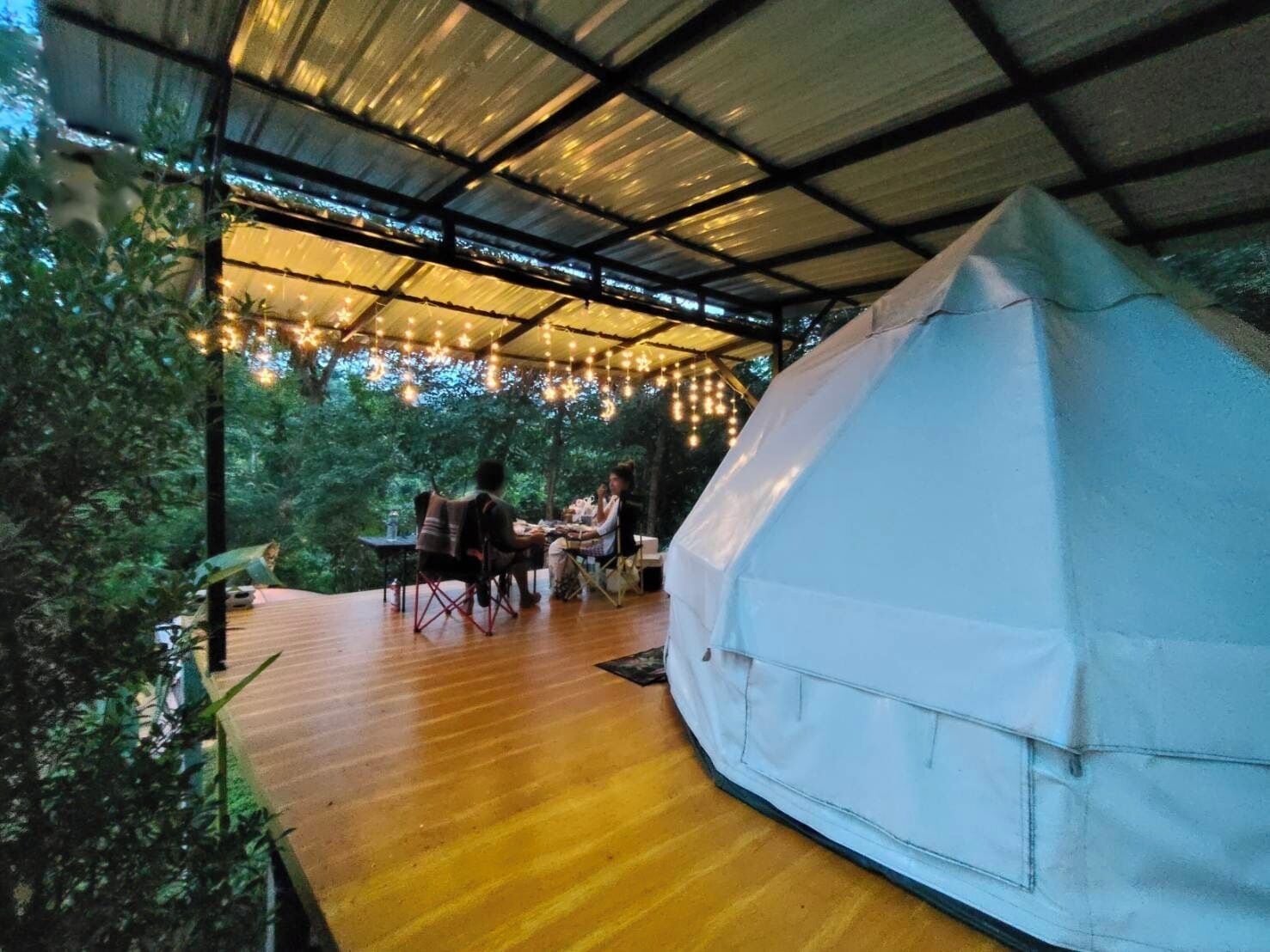 A covered outdoor area with a wooden deck, a white tent, and string lights.