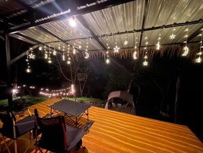 Un área de estar al aire libre con mesa y sillas bajo una estructura cubierta, decorada con luces colgantes.