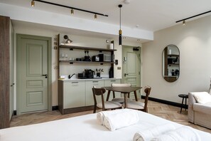 A modern hotel room with a bed, a dining table with chairs, a kitchen area with a microwave and coffee maker, and a large mirror on the wall. - Guestready - The Euston Hotel (London)